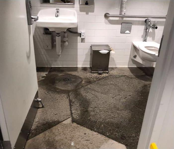 Sewage backup with contaminated materials on commercial bathroom floor